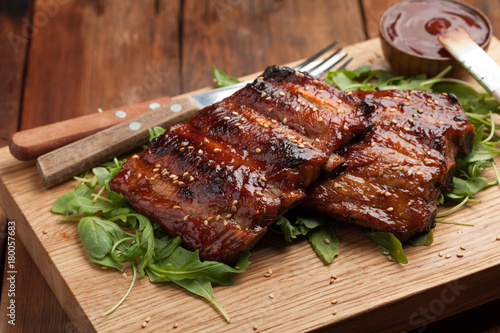 Closeup of pork ribs grilled with BBQ sauce and caramelized in honey on a bed of arugula. Tasty snack to beer on a wooden Board for submission on the old wooden background. Top view