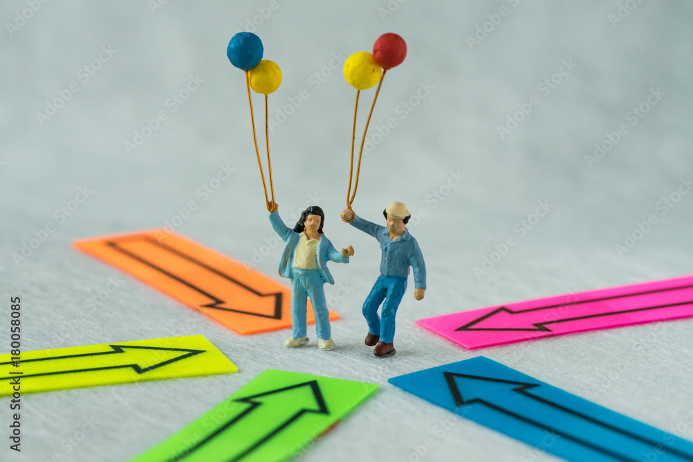 Miniature people figure couple holding balloons standing at the center of arrows pointing to them in all directions as people center concept