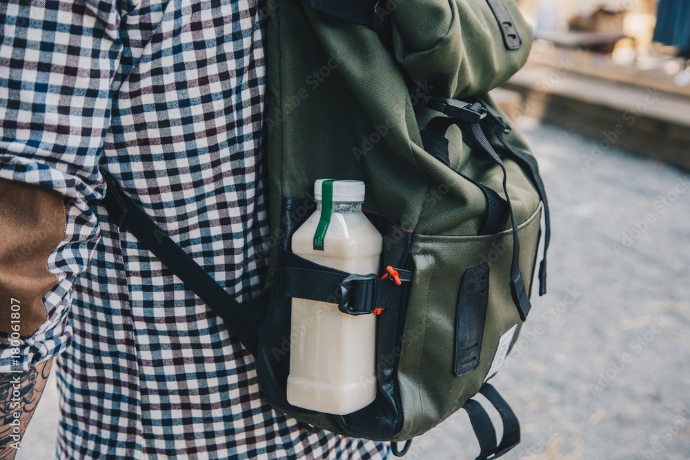 Obraz premium Side view shot. Close up man walking with plastic bottle of detox nutrition milk drink in backpack outdoor in the street.
