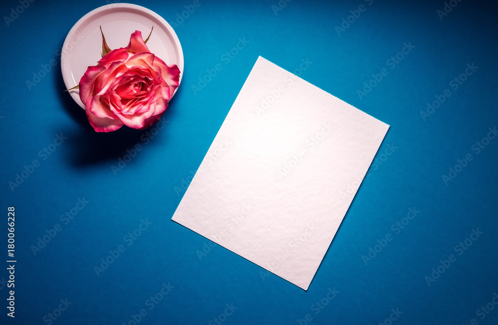 Painter workplace mockup. White sheet of watercolour paper on a blue background, beautiful colored roses in a white saucer. Art concept. Desk for the artist. Flat lay.