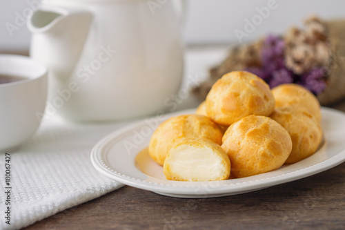 Obraz na plátne Homemade cream puffs or eclair or choux cream filled with vanilla custard cream on white plate put on wood table with copy space serve with tea in white pot or cup of coffee