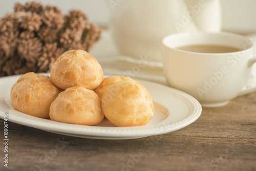 Homemade cream puffs or eclair or choux cream filled with vanilla custard cream on white plate put on wood table with copy space serve with tea in white pot or cup of coffee. French dessert.