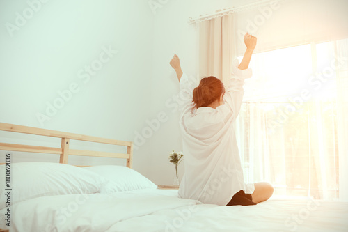 Young woman wake up in the morning and sitting on bed at window door side relaxing in holiday with sunlight, back side view