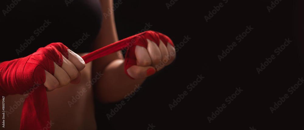 Fototapeta Kobieta sportowiec mieszanych sztuk walki owija ręce czerwonymi okładami bokserskimi. Pojedynczo na czarnym tle z miejsca na kopię. Silna ręka, gotowa do walki, aktywnych ćwiczeń i sparingów. Samoobrona kobiet.