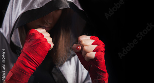 Female boxer makes a fight with a shadow, silver boxing robe and red boxing wraps, black background with copy space. Strong and confident, she will be a champion.