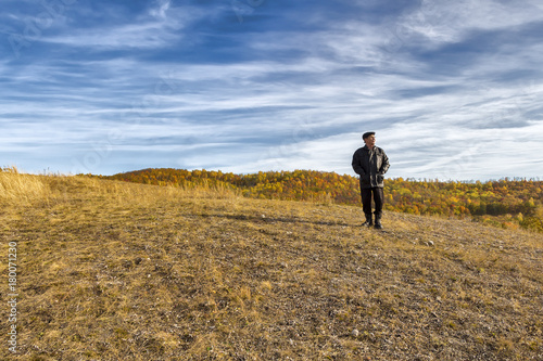 An elderly man stands on the top of a hill in the autumn period. © sv_production