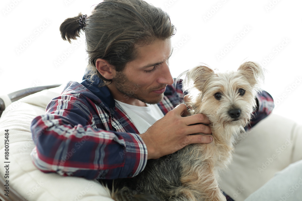 close-up of a smiling guy stroking his dog while sitting in a large armchair.