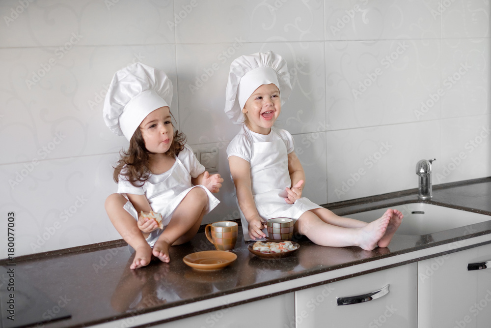 two little baker girls are drinking tea with a pabcakes in the kitchen two little baker girls are drinking tea with a pabcakes in the kitchen