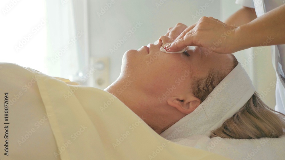 Cosmetologist is cleaning woman's face by cotton sponge at spa salon Cosmetologist is cleaning woman's face by cotton sponge at spa salon