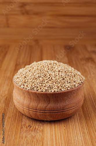 Quinoa in wooden bowl on brown bamboo board, closeup.