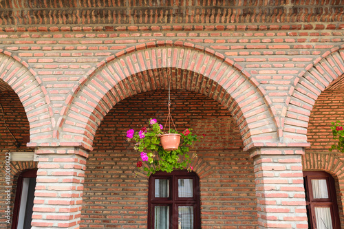 detail of red vintage brick arcades, brown windows frame and hanging geranium flower pot