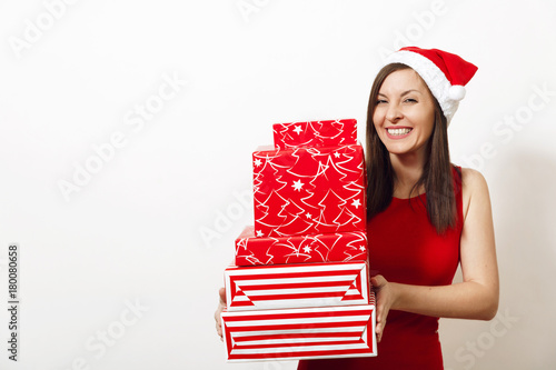 Beautiful caucasian young happy woman with charming smile dressed in red dress and Christmas hat holding gift boxes on white background. Santa girl with present isolated. New Year holiday 2018 concept photo