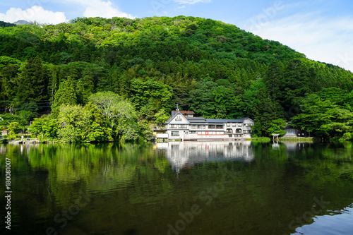 Beautiful abundant natural green mountain slope reflection on fresh lake Kinrinko with buildings during springtime