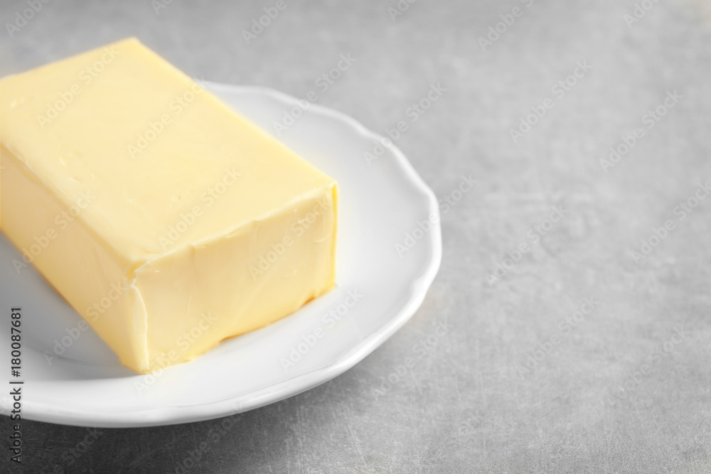 Plate with block of butter on grey background