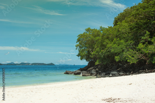 Beautiful tropical beach with sea view, black rocks with green trees