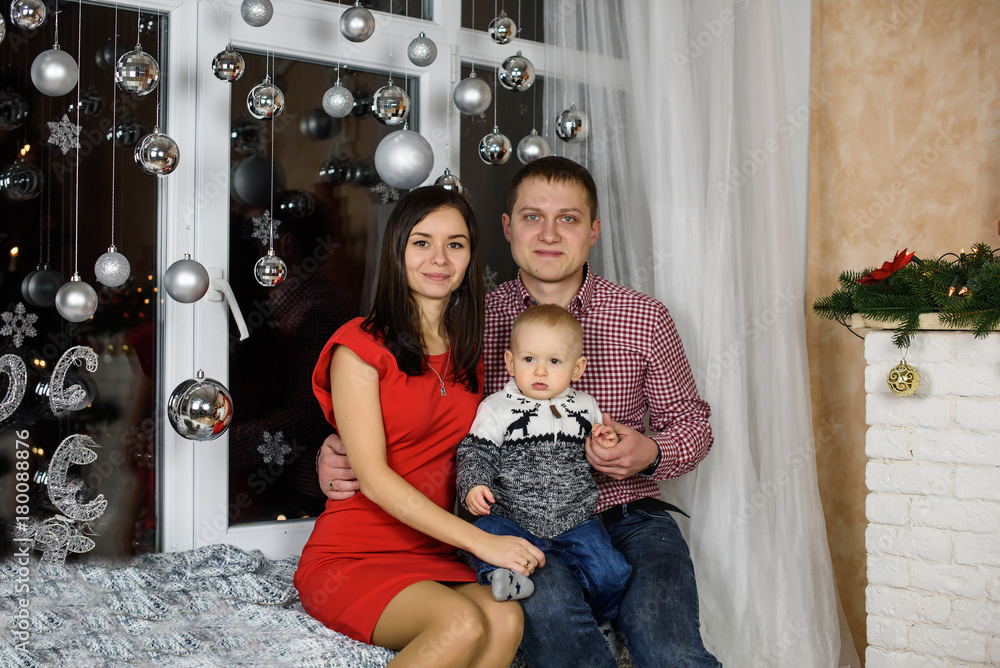 Portrait of happy family mother, father and adorable baby celebrate Christmas. New Year's holidays. Toddler with father and mother in the festively decorated room