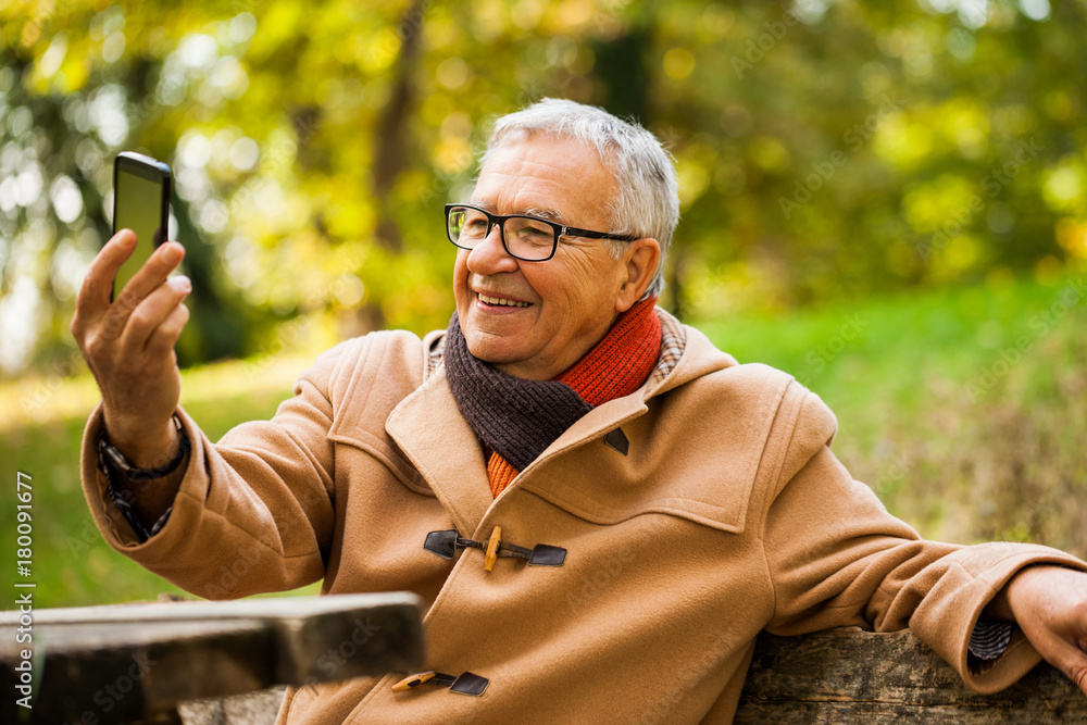 Happy senior man taking selfie in park in autumn. Happy senior man taking selfie in park in autumn.