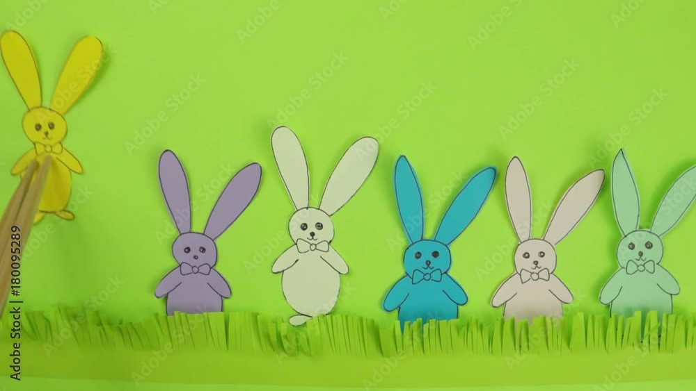 Multicolored figures of rabbits made of paper move on a green background Multicolored figures of rabbits made of paper move on a green background