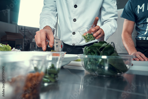 The chef prepares the dish. Sprinkle the salad with spices. Cooking. Professional kitchen. Salad dressing. Spices for salad