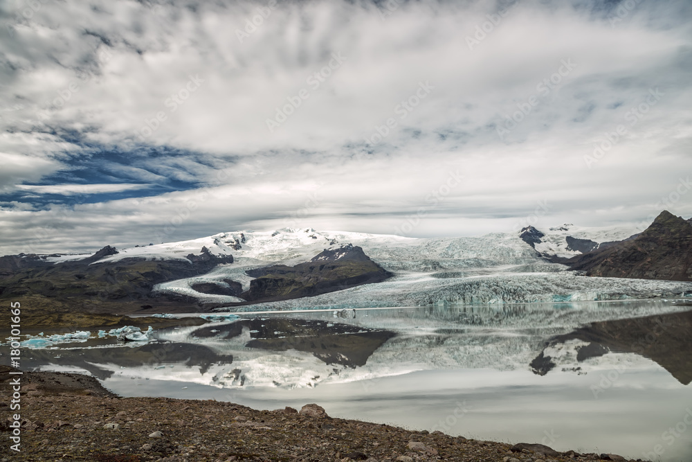 A view of the snow-capped mountains and a melting glacier on the shore of the lake. Iceland. Melting glaciers. Beautiful landscape of wild nature.
