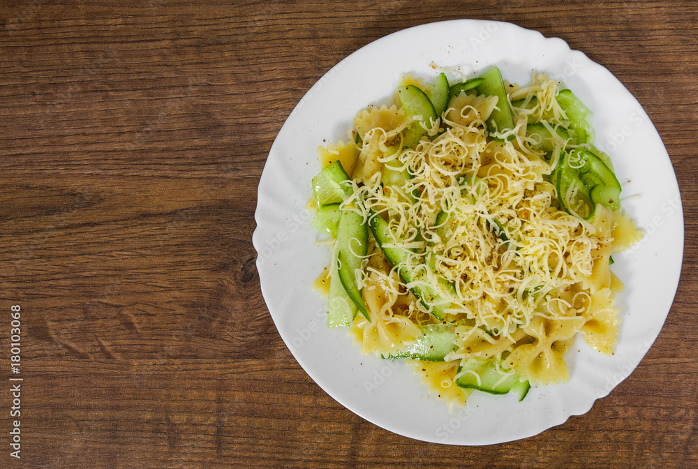 pasta farfalle salad with cucumber and cheese in plate on a wooden background. with copy space. top view pasta farfalle salad with cucumber and cheese in plate on a wooden background. with copy space. top view