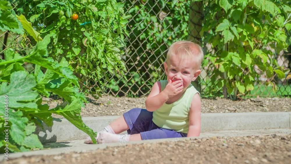 Cute baby girl sitting on the dirty floor, tasting small red tomato and does not really like its taste. Cute baby girl sitting on the dirty floor, tasting small red tomato and does not really like its taste.