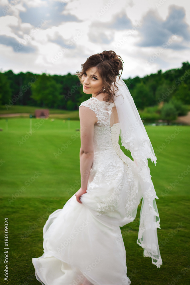 Attractive slender bride in a stylish white dress dancing on a green meadow in the nature