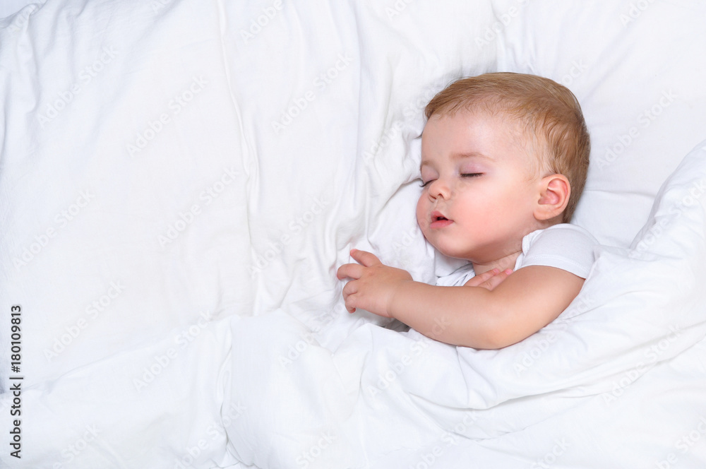 Cute one year old baby boy sleeping in a white bed

