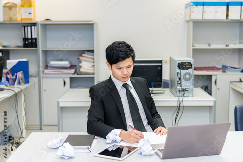 Asian handsome Businessman in suit work hard with crumped paper in the office,Young man stressed about the declining sales of the company.