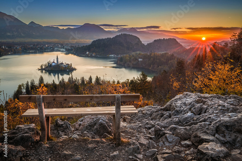 Bled, Slovenia - Beautiful panormaic skyline autumn view with hilltop bench and colorful sunrise of Lake Bled and Pilgrimage Church of the Assumption of Maria photo