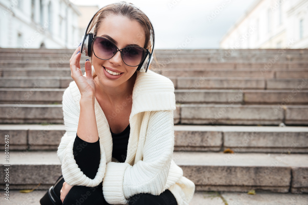 Young happy lady sitting on steps outdoors listening music