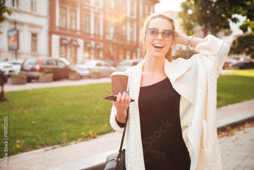 Young happy woman walking outdoors drinking coffee