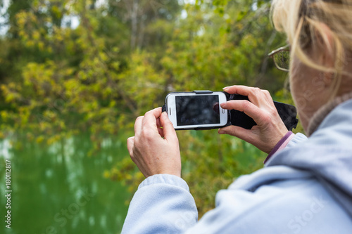A blonde woman using a phone takes a photo of a beautiful landscape