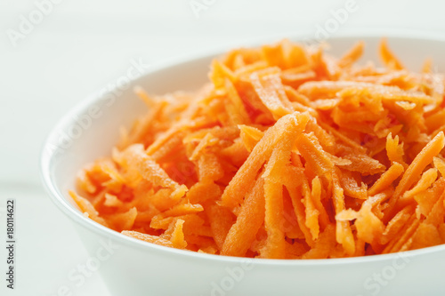 Grated fresh carrot in a white ceramic bowl, closeup shot