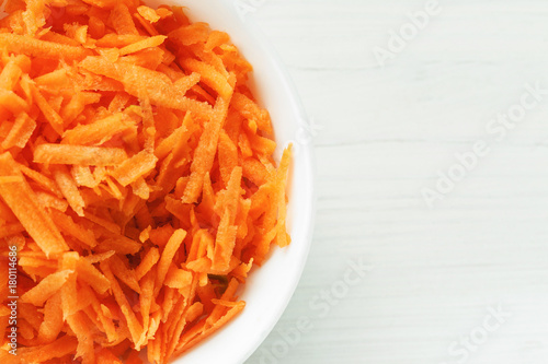 Grated fresh carrot in a white ceramic bowl top view, copy space