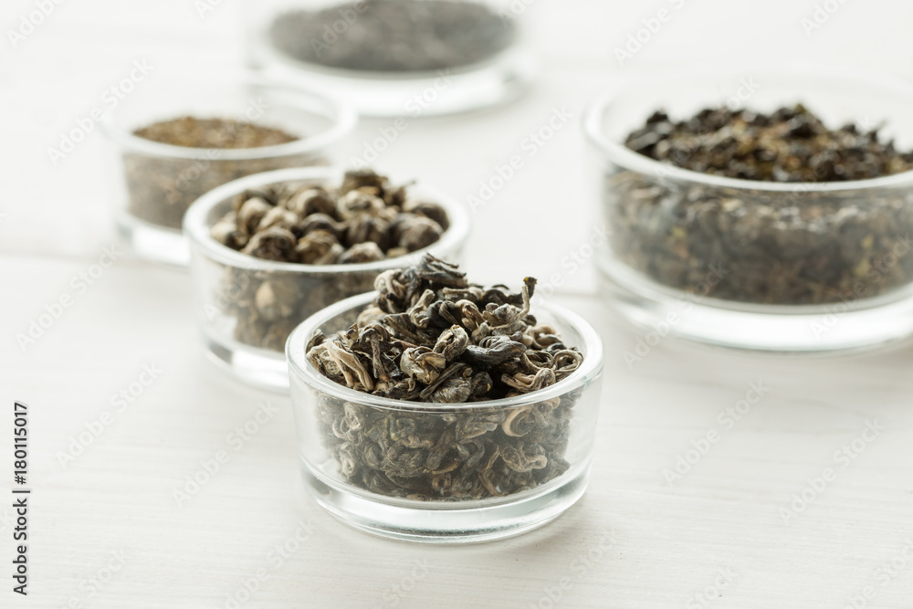 Different dry tea in a small glass dishes on a white wooden table Different dry tea in a small glass dishes on a white wooden table