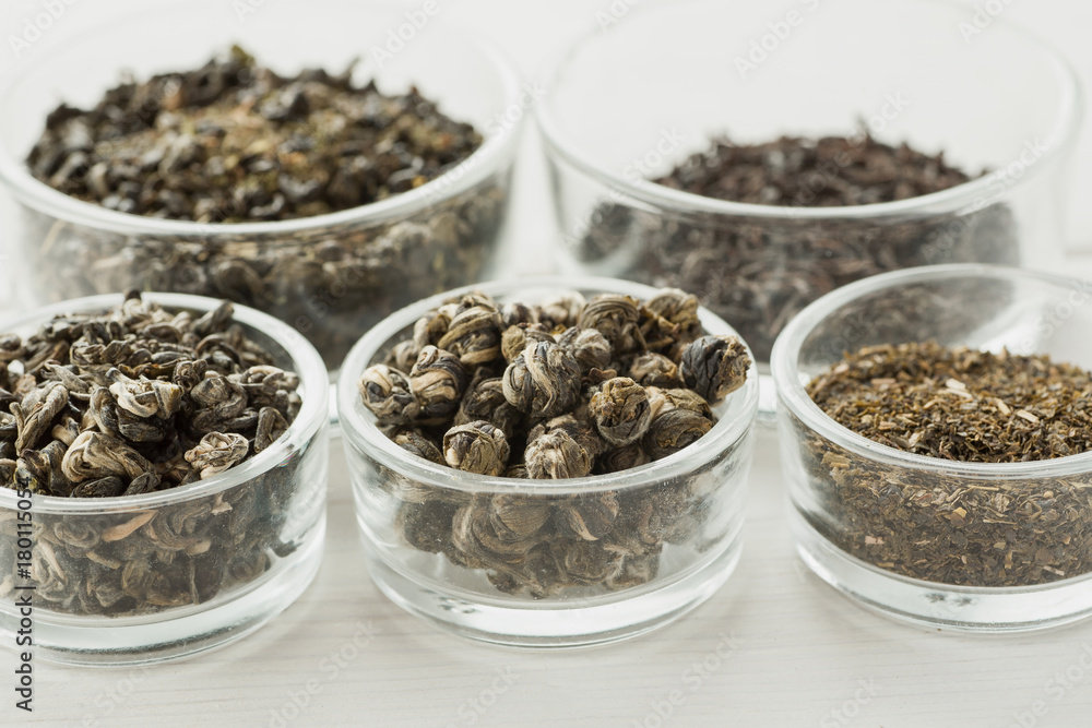 Different dry tea in a small glass dishes on a white wooden table Different dry tea in a small glass dishes on a white wooden table
