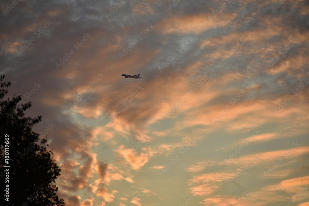 Airplane Flying Through A Cloudy Sunset Sky