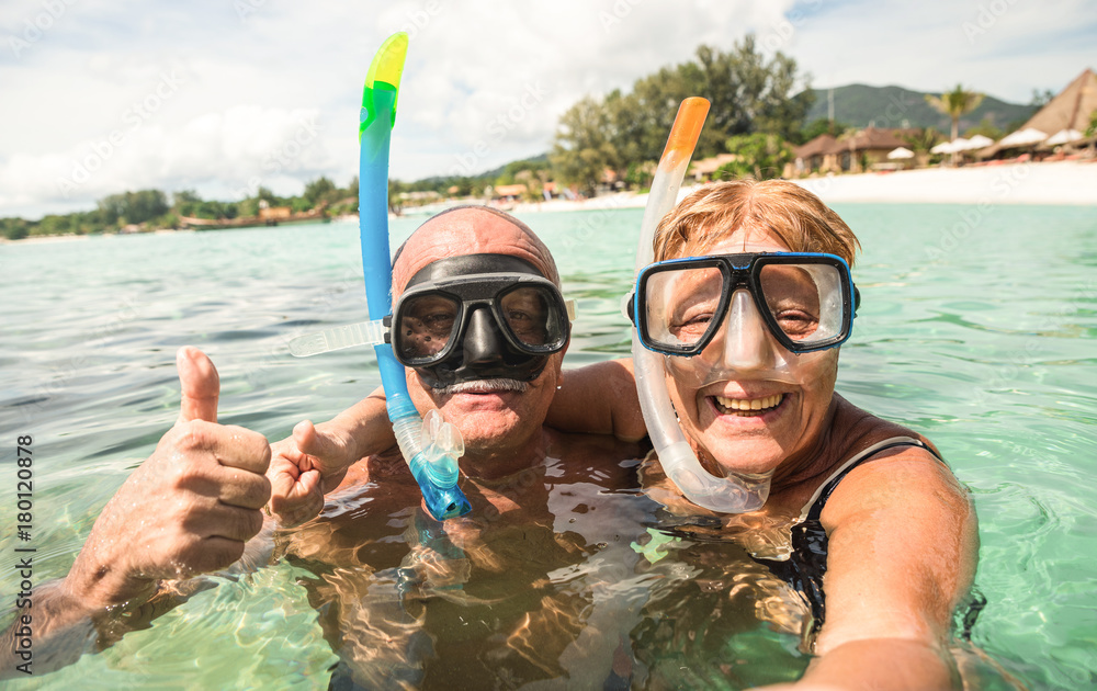 Fototapeta premium Senior happy couple taking selfie in tropical sea excursion with water camera - Boat trip snorkeling in exotic scenarios - Active retired elderly and fun concept around the world - Warm bright filter