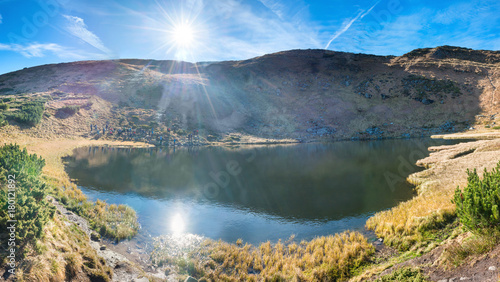 Panorama of mountains lake with reflection in blue water, morning light and shining sun