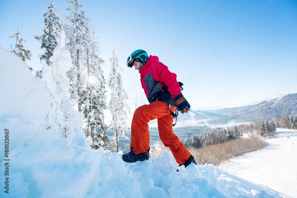 Snowboarder carrying his board walking in the winter mountains on sunny day copyspace active sports lifestyle recreation people