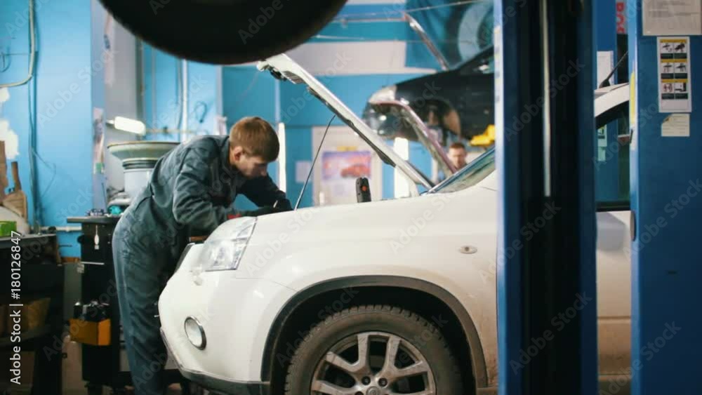 Mechanic male in automobile garage checking hood of a car Mechanic male in automobile garage checking hood of a car