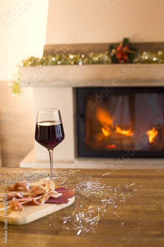 Fireplace decorated for Christmas. Glass of red wine and appetizer on wooden table and fireplace for background.