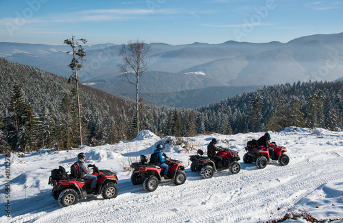 Four ATV riders on off-road quad bikes on snow at top of the mountain in winter
