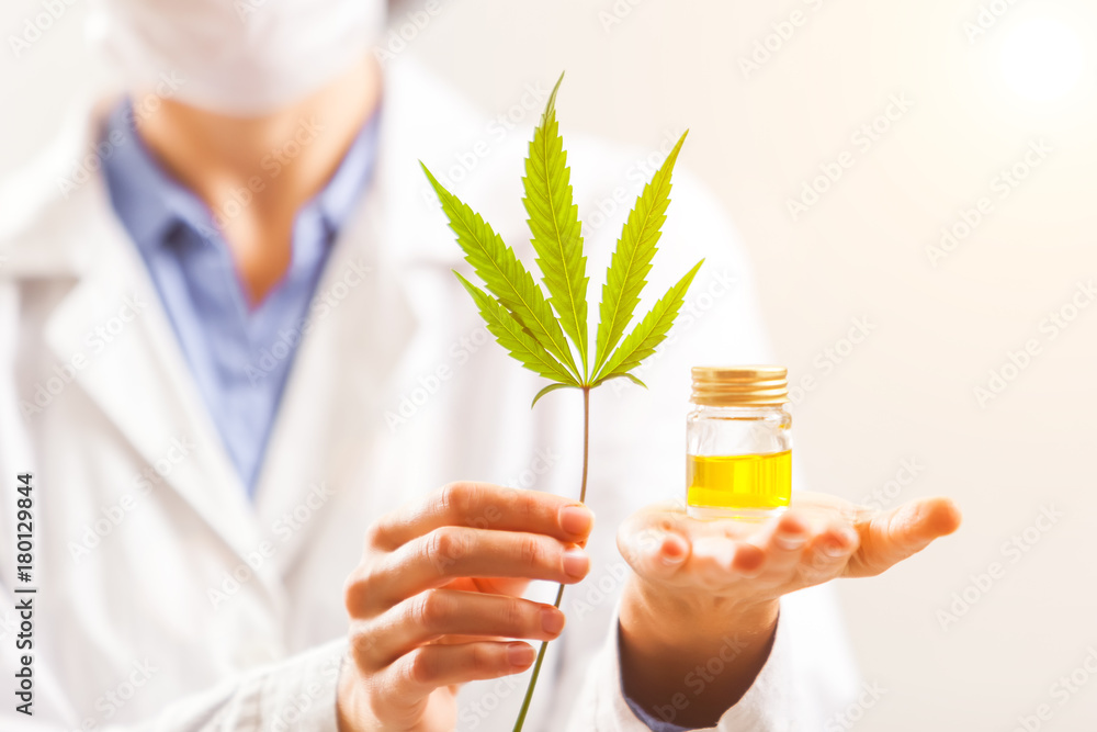 Woman doctor holding a cannabis leaf and oil Woman doctor holding a cannabis leaf and oil