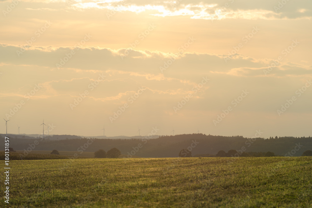 Beautiful, hazy landscape at sunset, with wind turbines in the background. Agriculture mixed with renewable energy. Representing hope for future generations. Hosingen, Luxembourg.