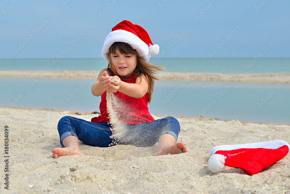 Obraz premium Cute little girl celebrating Christmas and New Year holidays on the beach, playing with sand