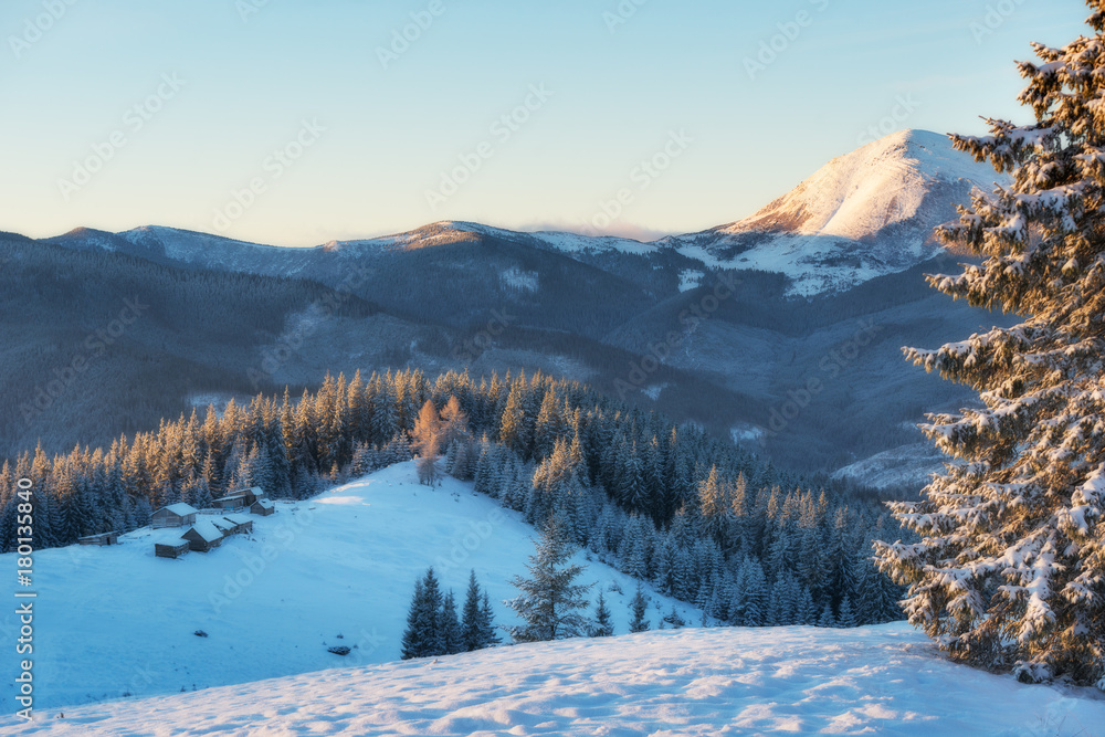 Fantastic sunset over snow-capped mountains and wooden chalets. In anticipation of the holiday. Dramatic scenes. Carpathian, Ukraine, Europe.
