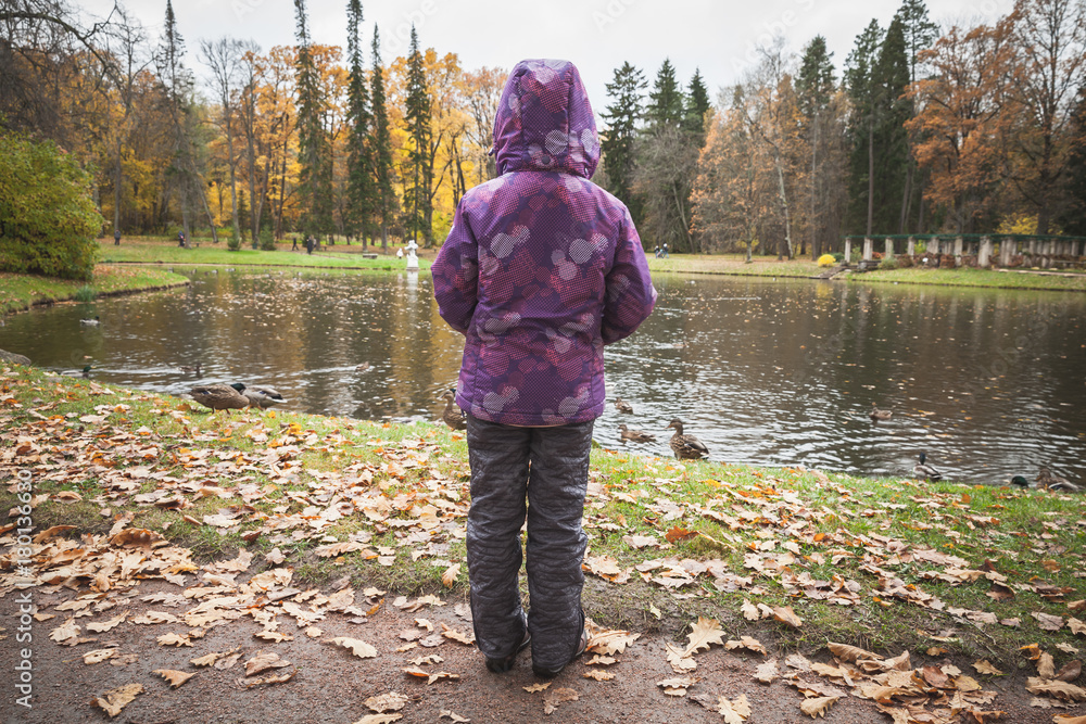 Little girl stands near lake coast in autumn park Little girl stands near lake coast in autumn park