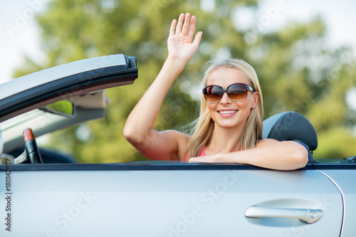 happy young woman in convertible car waving hand
